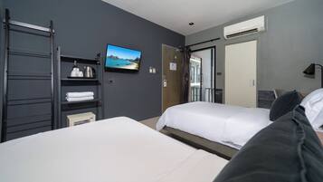 Quarto de hotel com duas camas, televisão, prateleira com amenities e ar condicionado.