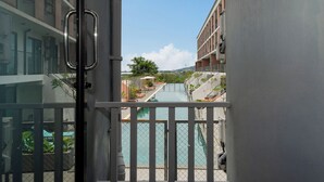A balcony with a pool, a view of a building, and a clear sky. - Dent Station Residence (Chalong)