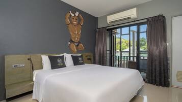 Habitación de hotel con cama, aire acondicionado fijo en la pared, ventana con cortinas y vista a follaje exterior.