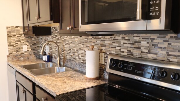 A kitchen with a stainless steel microwave, double sink, granite countertop, and a black oven. - Cozy Stylish 2 BR Home w / Relax & Enjoy (Owensboro)
