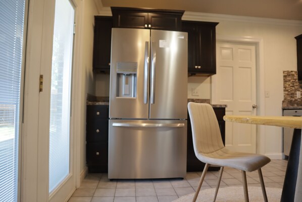 Una cocina con un refrigerador de acero inoxidable, armarios oscuros, una silla de color claro y piso de baldosas.