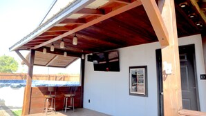 A covered outdoor area with a wooden deck, two bar stools, and a door. - Cozy Stylish 2 BR Home w / Relax & Enjoy (Owensboro)