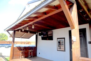 Un espacio al aire libre cubierto con una terraza de madera, dos taburetes de bar y una puerta.