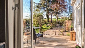 Eine Holzterrasse mit Gartenmöbeln, ein Garten mit Bäumen und Pflanzen und Blick auf eine ländliche Landschaft.