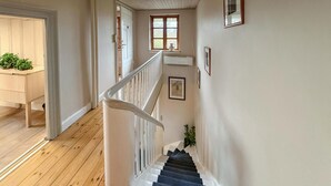 Eine Treppe mit weißen Geländern, Holzdielen und einem Fenster mit einer Vase.