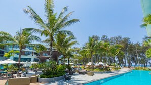 A resort pool area with lounge chairs, umbrellas, and palm trees. - Unit 2303 Beachfront | Pool-Facing + Sea View (Choeng Thale)