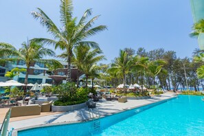 A resort pool area with lounge chairs, umbrellas, and palm trees. - Unit 2303 Beachfront | Pool-Facing + Sea View (Choeng Thale)