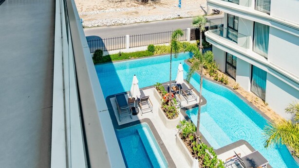 A modern hotel with a pool, outdoor seating, and a view of the beach and trees. - Unit 2303 Beachfront | Pool-Facing + Sea View (Choeng Thale)