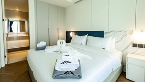 A hotel room with a bed, a nightstand, a mirror, a built-in wardrobe, and a bathroom. - Unit 2303 Beachfront | Pool-Facing + Sea View (Choeng Thale)