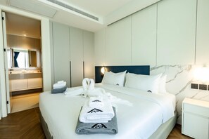A hotel room with a bed, a nightstand, a mirror, a built-in wardrobe, and a bathroom. - Unit 2303 Beachfront | Pool-Facing + Sea View (Choeng Thale)