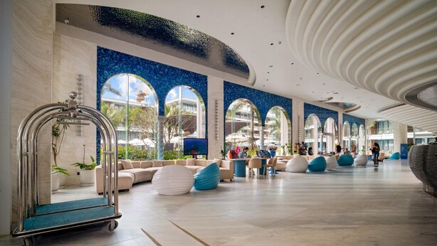 En rymlig lobby med modern design, med en stor sittgrupp, en servicevagn och utsikt över utomhusområdet genom stora fönster.