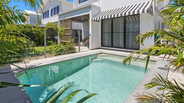 Ett modernt hus i två våningar med en swimmingpool, stora fönster och en täckt uteplats.