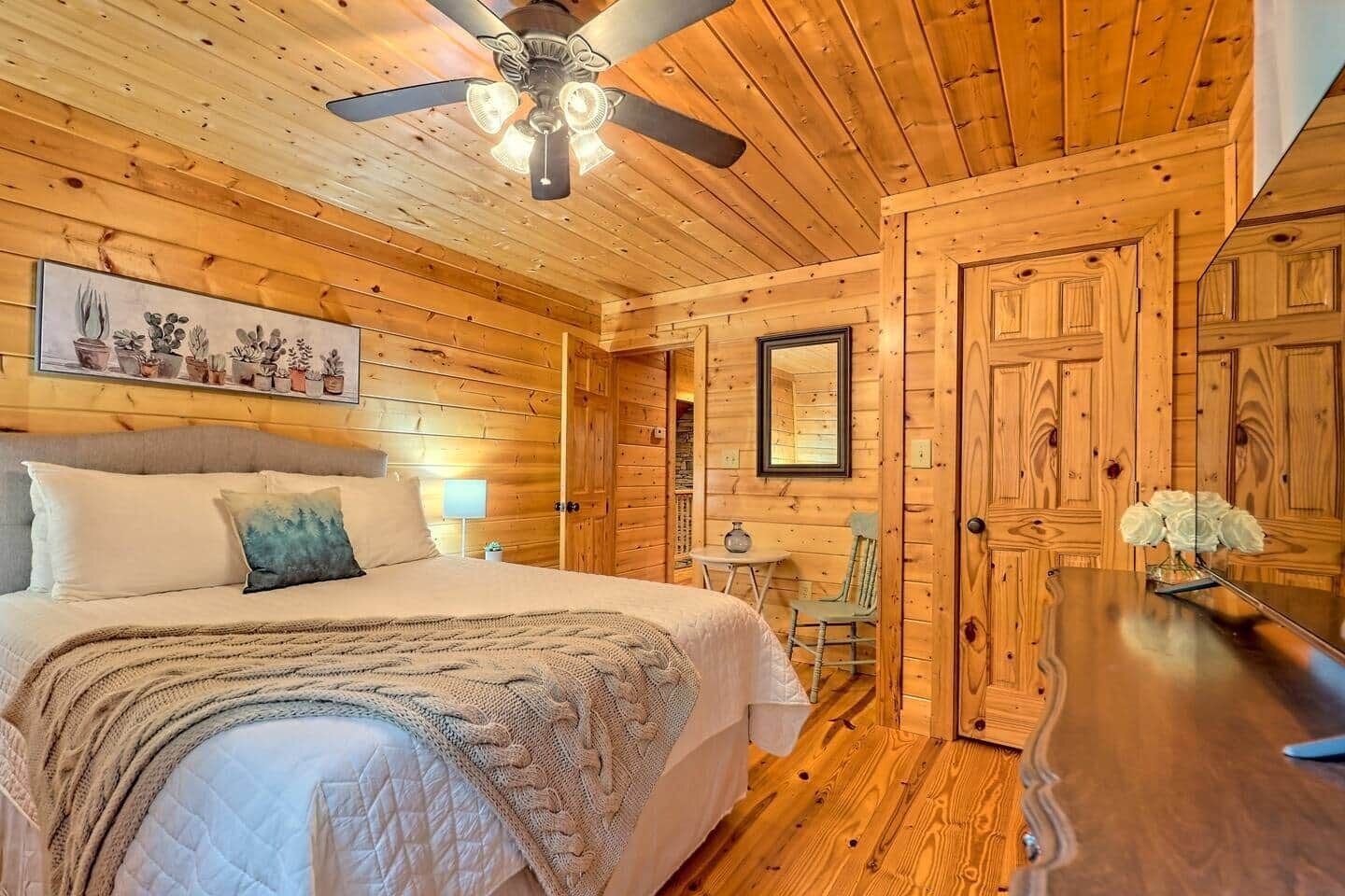 Een houten cabinestijl interieur met een bed, een plafondventilator, een eettafel en een stoel.
