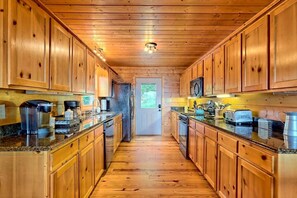 A wooden interior with a kitchen, wooden cabinets, granite countertops, and a central door. - Mountain View Log Cabin, Game Room, Dog Friendly (Rabun County)