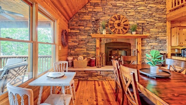 Een gezellig interieur van een chalet met een stenen muur, houten plafond, een open haard en een eethoek met stoelen en een tafel.