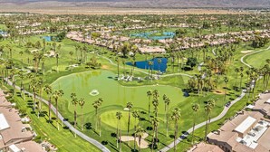Luftaufnahme eines Golfplatzes mit mehreren Wasserhindernissen, umgeben von Wohngebäuden und Palmen.