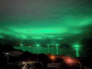 Ein Nachtblick auf ein Gewässer mit einem grünen Polarlicht darüber und einer Brücke in der Ferne.