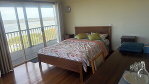A bedroom with a wooden bed, a nightstand, a dresser, and a view of a body of water through a balcony. - Room-pillais B & B, Private Room Attach (Albany)