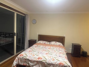 Ein Schlafzimmer mit Bett, Nachttisch, Kommode, Wanduhr und einer Schiebeglasdoor.