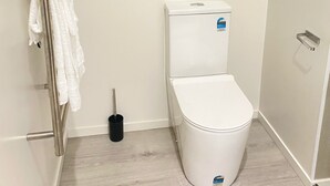 A small, clean bathroom with a toilet, a towel rack with white towels, a window, and a door. - Fabulous residence in New Plymouth (New Plymouth)
