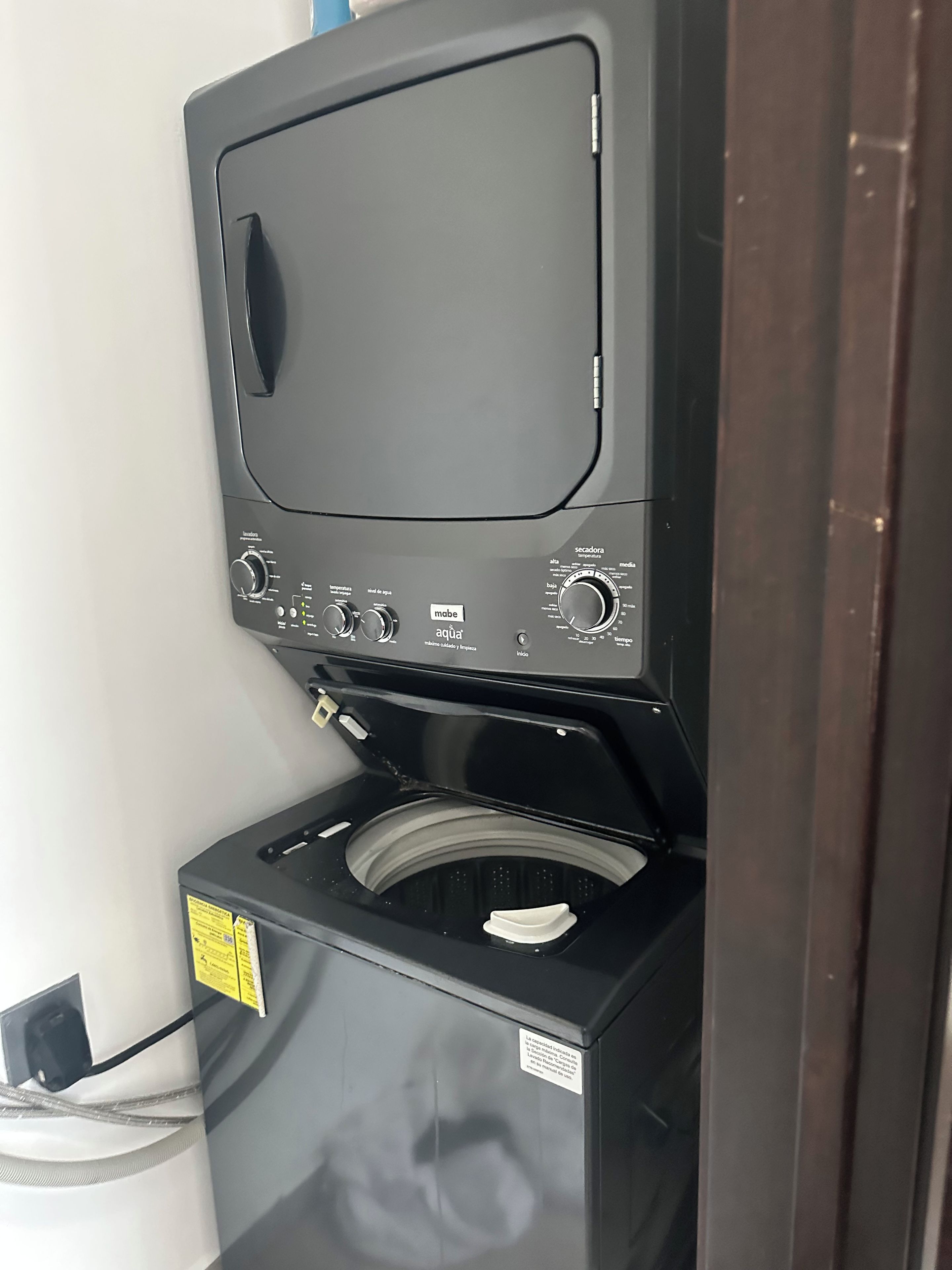 Vue de face d’un lave-linge, avec ses boutons de commande, son arrivée d’eau et une étiquette indiquant les instructions.