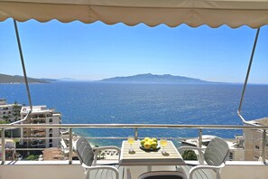 A balcony with a table, two chairs, and a plate of lemons and glasses of drink. - Panorama View Apartment In Saranda - 271, Sarandë, Albania (Sarandë)