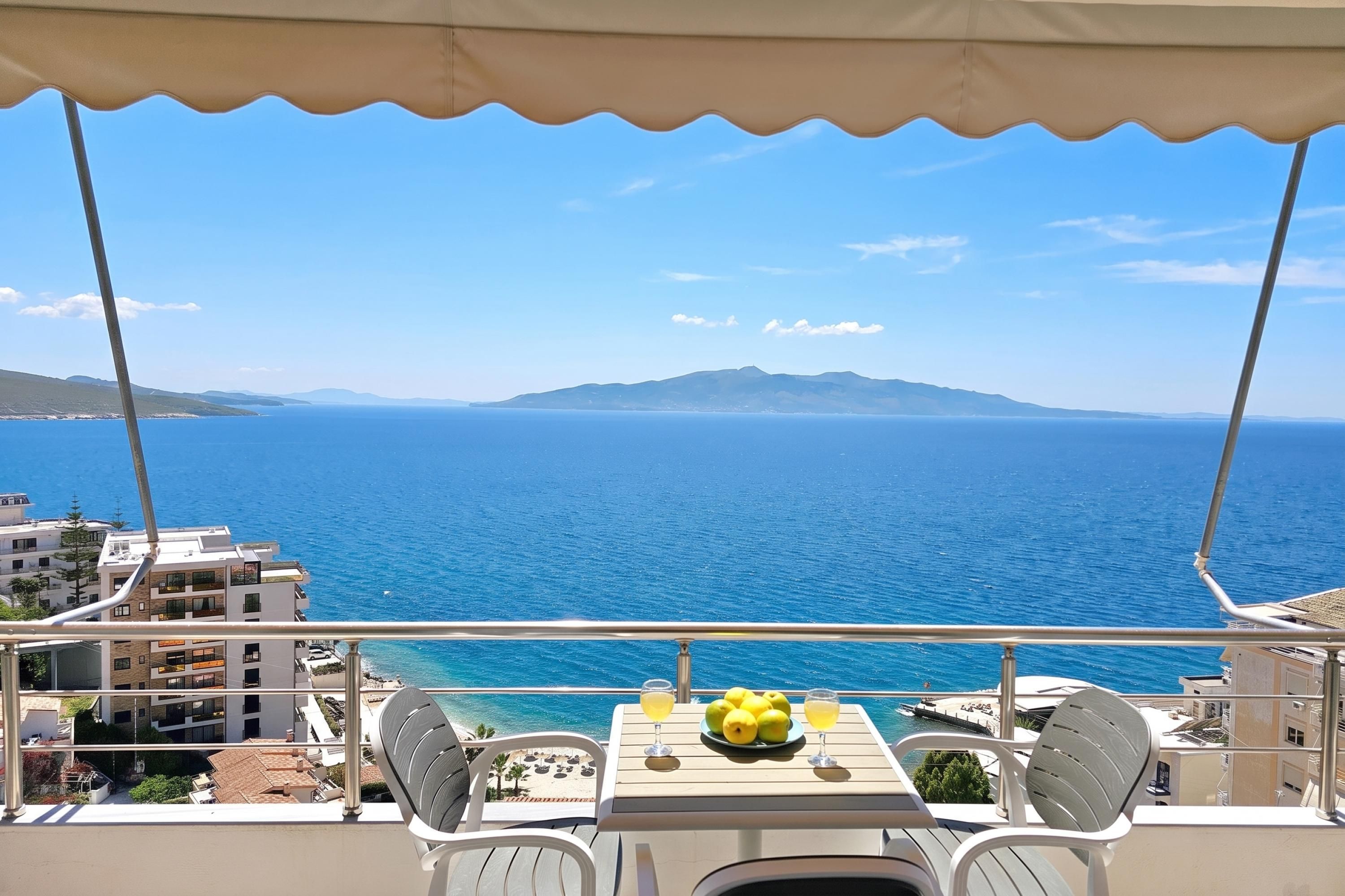 Ein Balkon mit Tisch, Stühlen und Blick auf das Meer und ferne Berge.