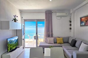 A modern living room with a television, sofa, and a balcony with a view of the sea. - Panorama View Apartment In Saranda - 271, Sarandë, Albania (Sarandë)