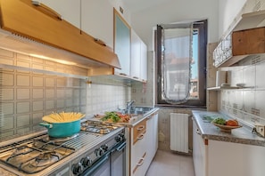 Angolo cottura compatto con piano cottura a gas, pentola di pasta e finestra vista.
