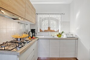 A kitchen with a gas stove, a sink, and a window with a curtain. - Toscolano Olive House, Toscolano Maderno, Italy (Toscolano Maderno)