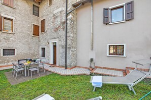A courtyard with a table and chairs, a small garden, and a building with multiple windows and a door. - Toscolano Olive House, Toscolano Maderno, Italy (Toscolano Maderno)