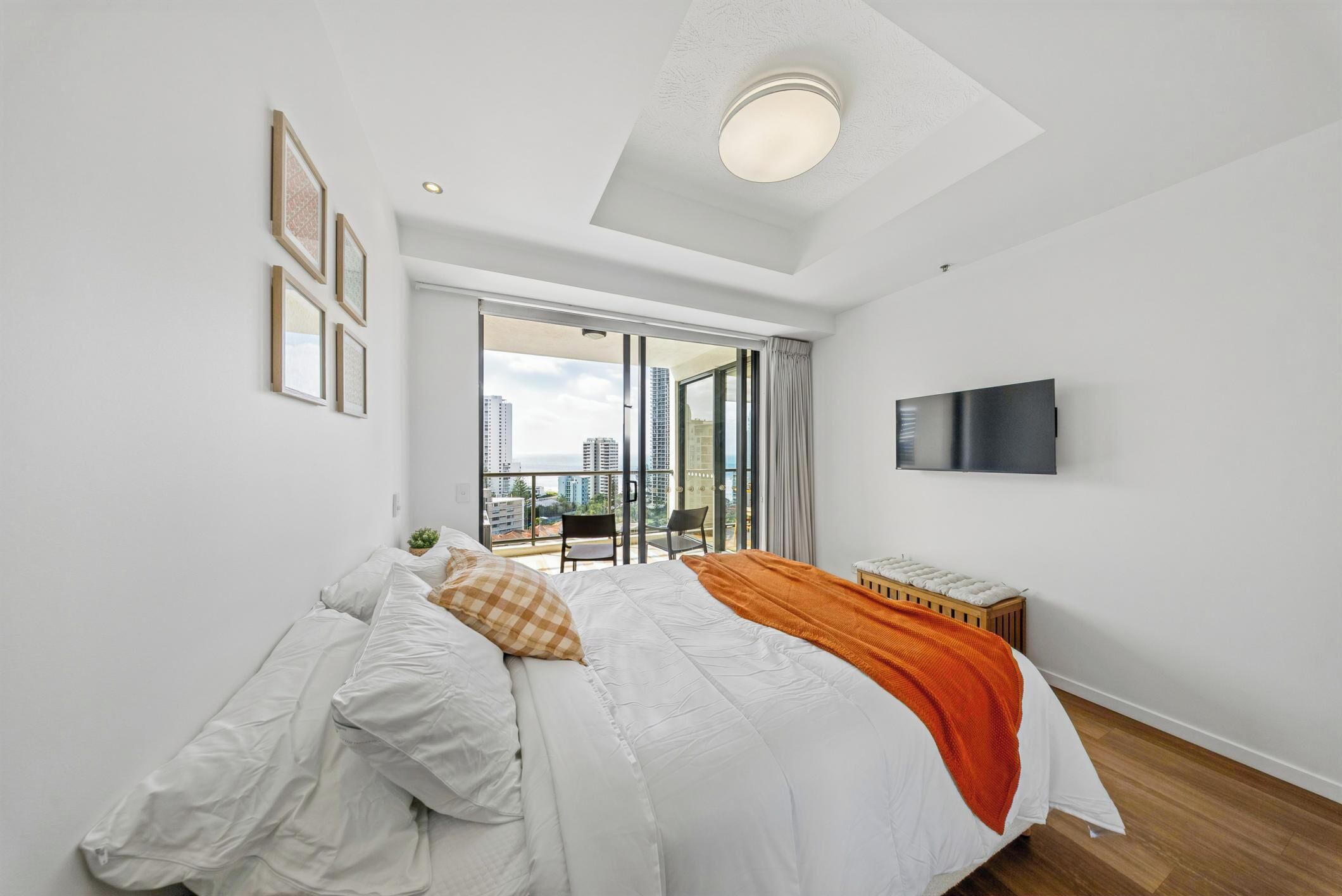 Ein modernes Schlafzimmer mit einem großen Bett, einem Fernseher und einem Balkon mit Blick auf die Stadt.
