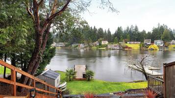Une propriété située au bord du lac, dotée d’une terrasse en bois, d’un petit abri de jardin et offrant une vue sur les maisons de l’autre côté de l’eau.