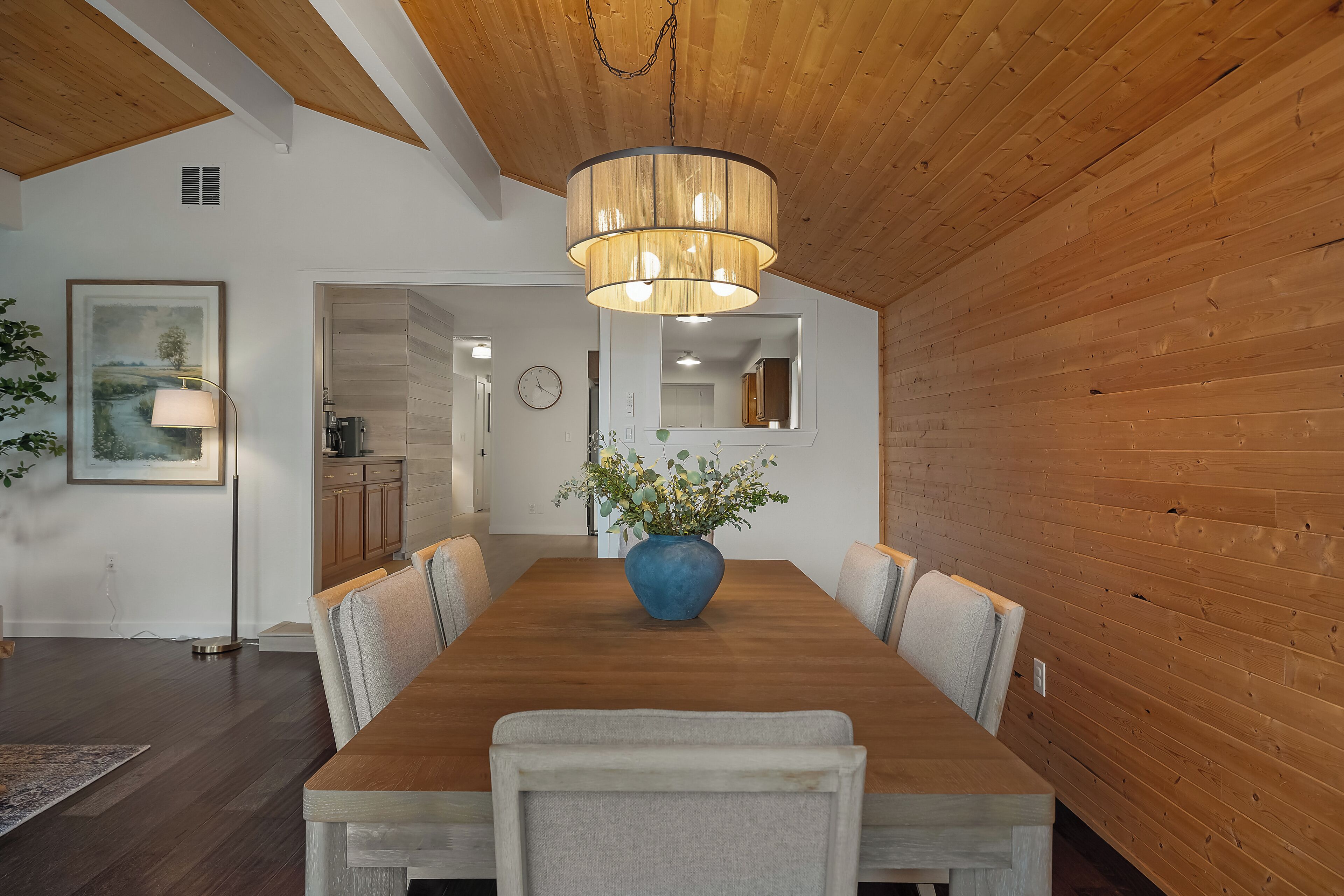 Un coin repas avec une table en bois, des chaises, un vase bleu rempli de fleurs et un luminaire suspendu.