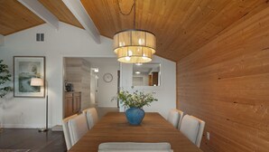 Ein Essbereich mit einem Holztisch, Stühlen, einer blauen Vase mit Blumen und einer Pendelleuchte.