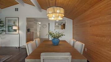 Un coin repas avec une table en bois, des chaises, un vase bleu rempli de fleurs et un luminaire suspendu.