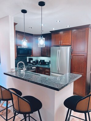 A modern kitchen with granite countertops, stainless steel appliances, wooden cabinets, and pendant lighting.