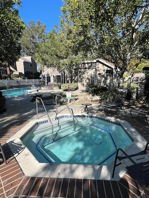 A swimming pool with a hot tub, surrounded by lounge chairs and a stone wall.