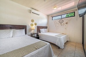 Una habitación con dos camas, una mesita de noche, aire acondicionado de pared, una ventana con vistas y una lámpara en el techo.