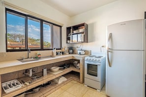 Cocina compacta con estufa, horno, refrigerador y ventana con vista a edificios.