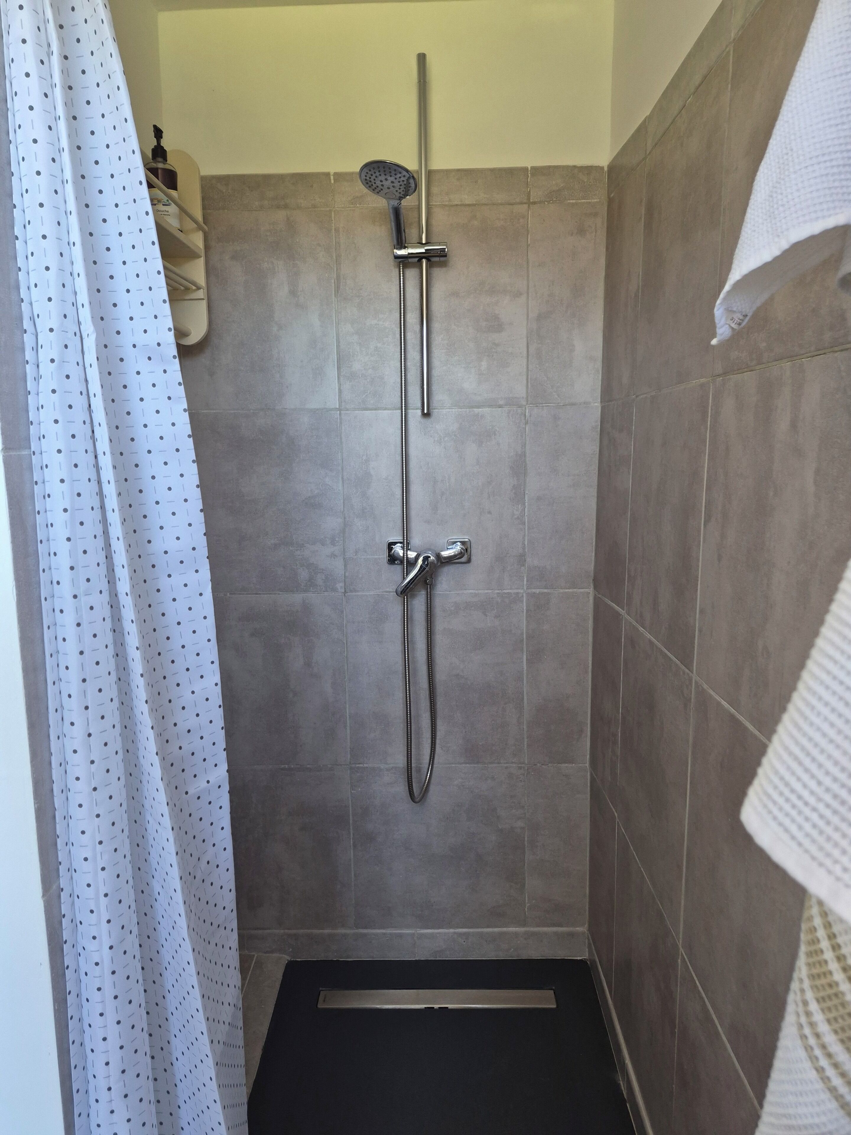 Eine Dusche mit Handbrause und Wandarmatur, mit Fliesenwänden und einer Duschmatte.