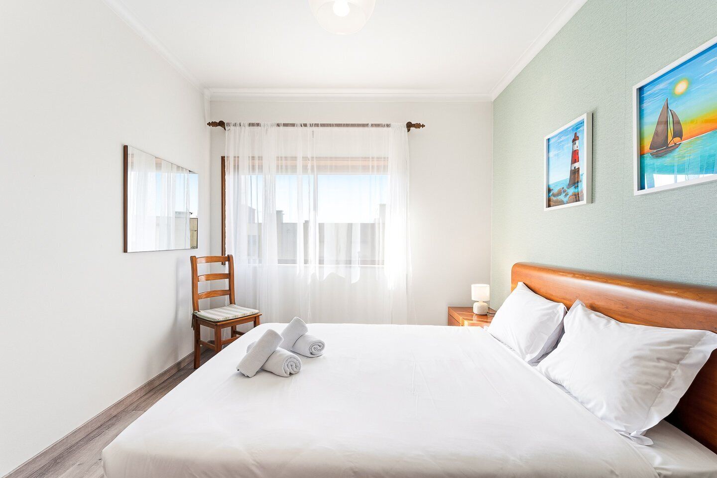Habitación de hotel con una cama, una silla, una mesita de noche y una ventana con cortinas traslúcidas.