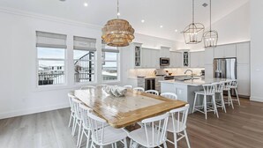 Une cuisine moderne avec des meubles blancs, un îlot central et un coin repas comprenant une table en bois et des chaises blanches.