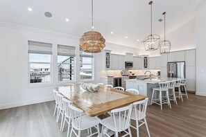 A modern kitchen with white cabinetry, a central island, and a dining area with a wooden table and white chairs. - Southern Comfort, Navarre Beach FL (Navarre)