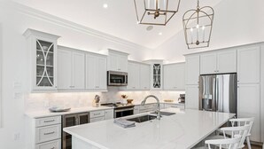 Une cuisine moderne avec des meubles blancs, des appareils en acier inoxydable et un îlot central doté de tabourets de bar.