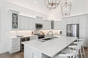 A modern kitchen with white cabinetry, stainless steel appliances, and a central island with bar stools. - Southern Comfort, Navarre Beach FL (Navarre)