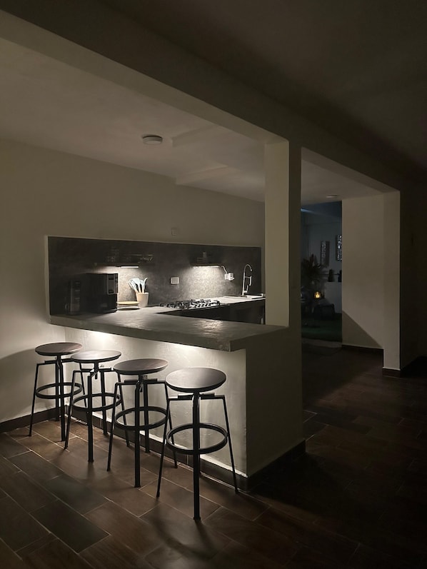 A modern kitchen with a central island, bar stools, and a view into another room.