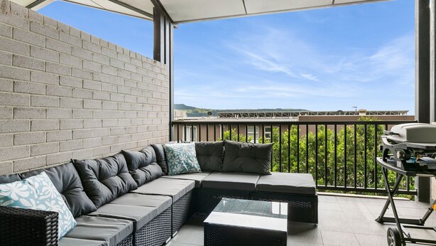 En balkon med en hjørnesofa, et lille bord og en grill.