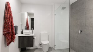 Et moderne badeværelse med en hvid vask, toilet, glasbrusekabine og et mørkt træskab.