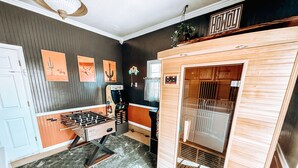 A room with a foosball table, a kitchen area, and a wooden cabinet with a glass door. - Centrally Located, Family friendly Home- With Game Room and Infrared Sauna (Farmington)